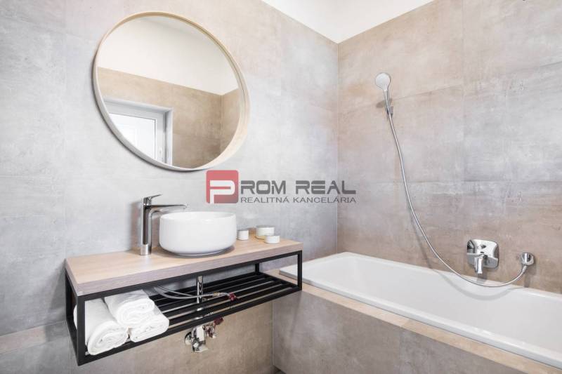A bathroom with a sink, bathtub, and round mirror in a 3-room apartment.