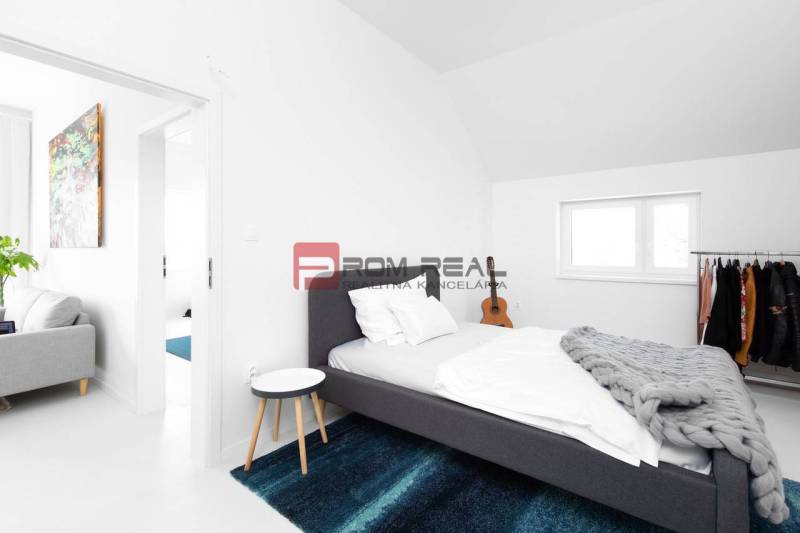 A bedroom with a bed, a blue carpet, and a coat rack in a three-room apartment.