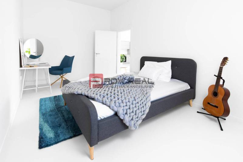 A simple bedroom with a bed, a table, a chair, and a guitar in a 3-room apartment.