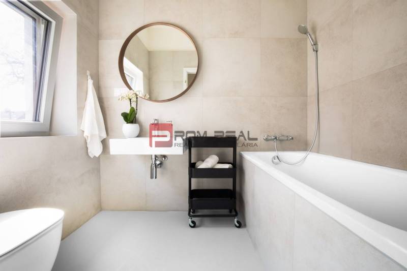 A bathroom in a 3-room apartment with a bathtub, a mirror, and a window, decorated with a flower.