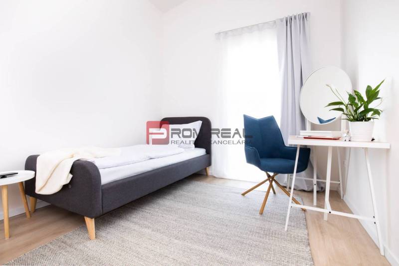 A bright room with a gray bed, a blue chair, and a table in a 3-room apartment.