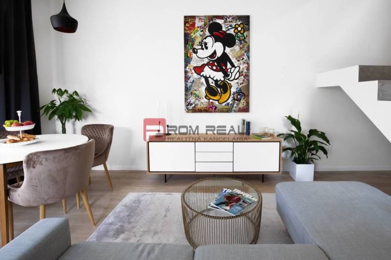 Living room with a colorful painting, comfortable seating, and a table in a three-room apartment.