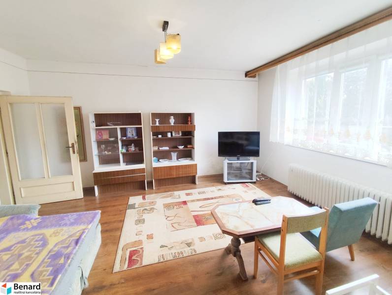 Living room in a family house with older furniture, a television, and a large window.