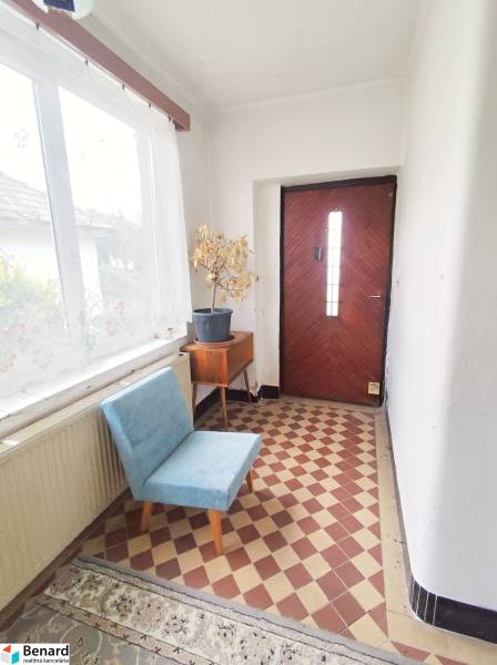 Entrance hall in a family house with a flower pot, a blue chair, and checkered tiles.