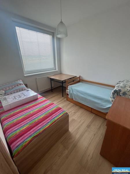 A room in a 3-room apartment with two beds, a table, and wooden flooring.
