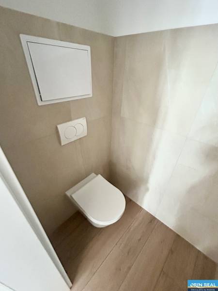 A toilet with concealed flushing in a 3-room apartment, surrounded by light tiles and wooden flooring.