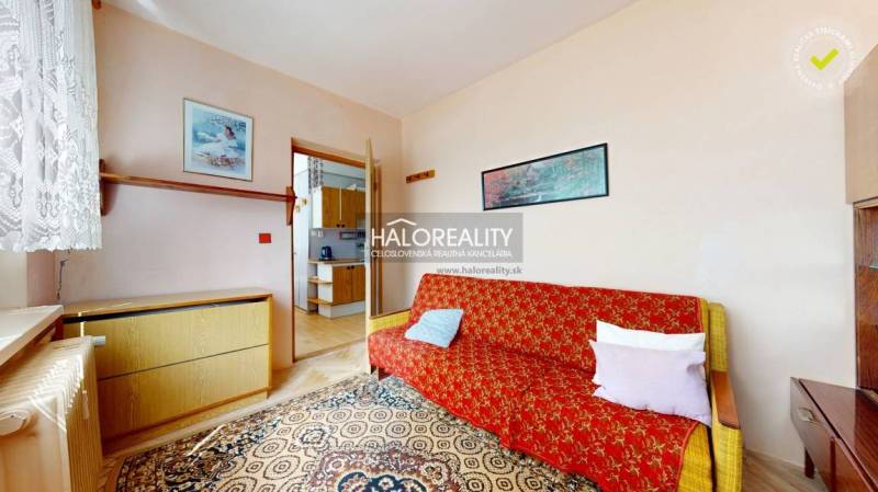 A room in a 4-room apartment with a sofa, carpet, and entrance to the kitchen.