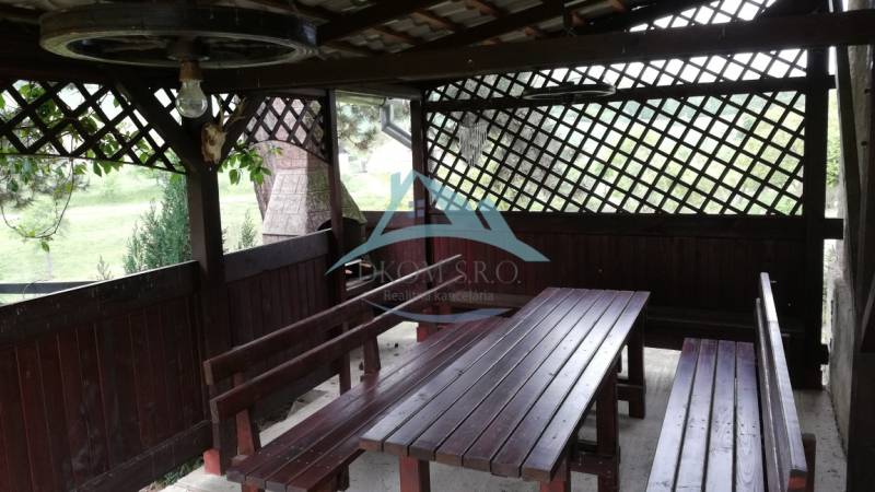 A wooden gazebo with benches located in the garden of a family house.