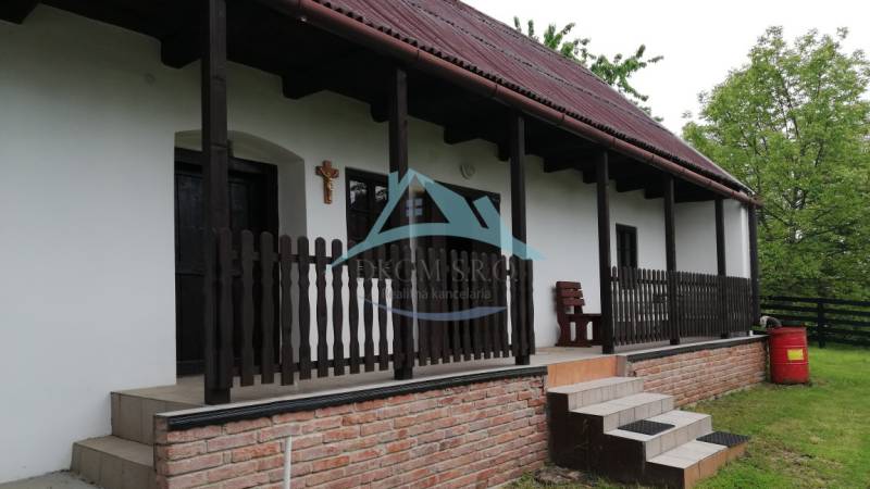Family house with a terrace, wooden fence, and brick foundation in a natural setting.