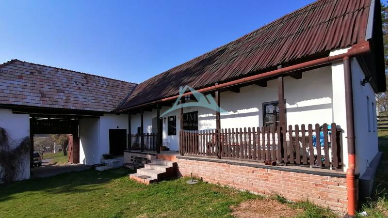 Family house with a porch, wooden beams, brick foundation, and a large grassy garden.
