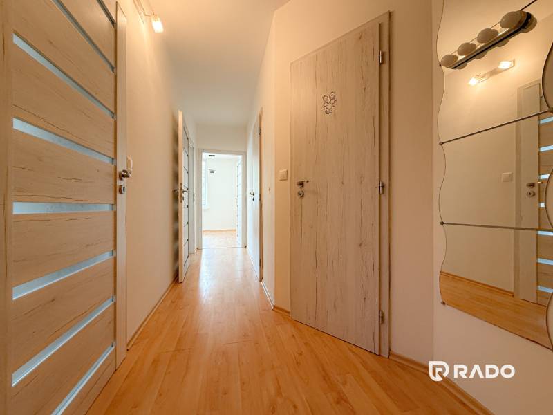A hallway in a 3-room apartment with wooden flooring, white doors, and a mirror.