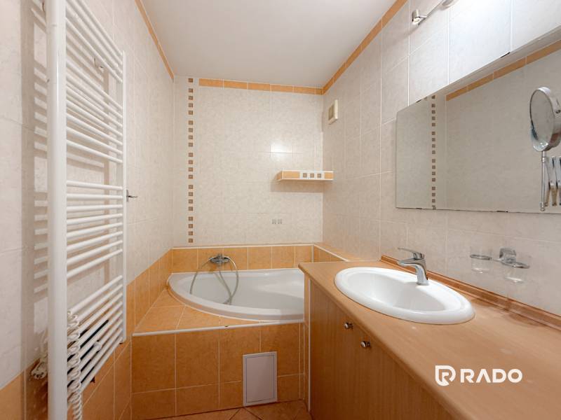 A bathroom in a 3-room apartment with a corner bathtub, sink, and radiator.