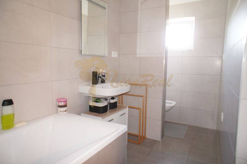 A bathroom in a family house with a bathtub, a sink, a shower corner, and large-format tiles.