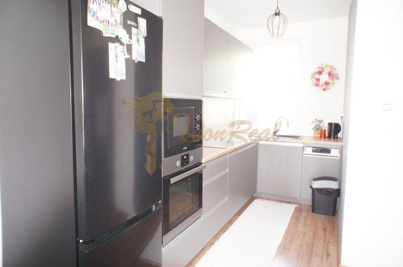 A kitchen in a family house with a black refrigerator and a built-in oven on a wooden floor.
