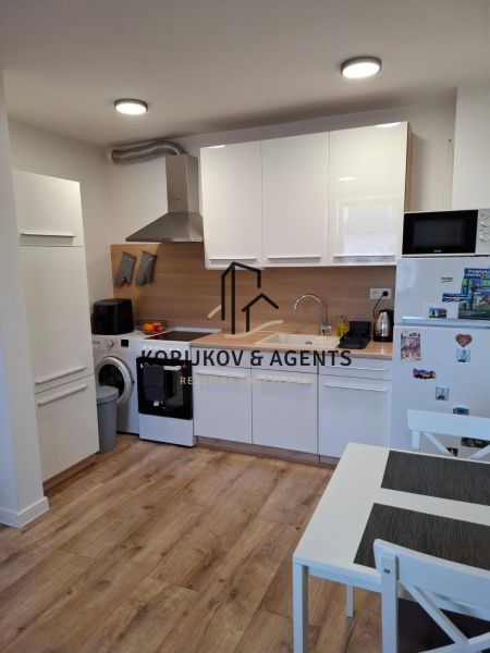 A kitchen in a 2-room apartment with white furniture and a wooden decor floor.