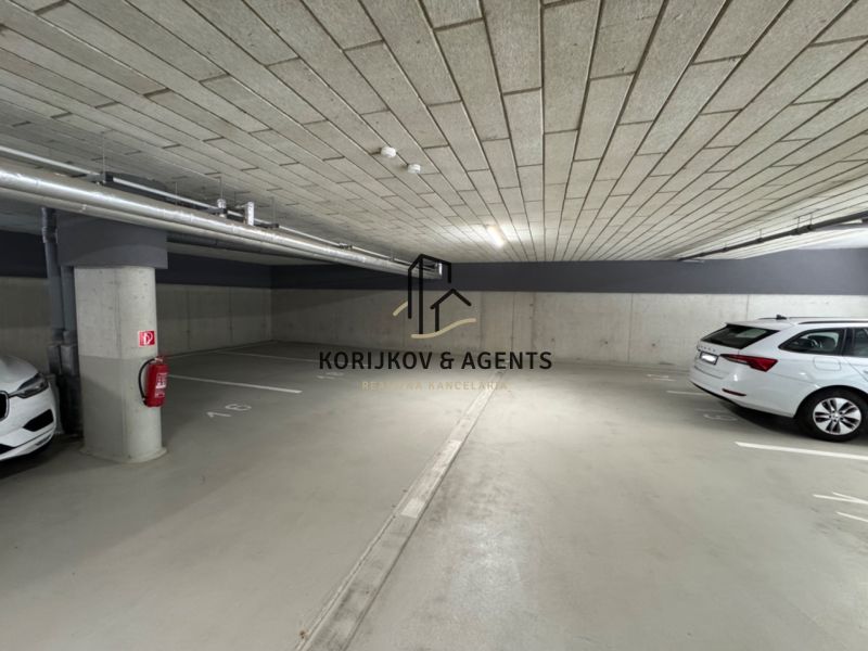 Underground garage with parking spaces, concrete walls and ceiling, two parked vehicles.