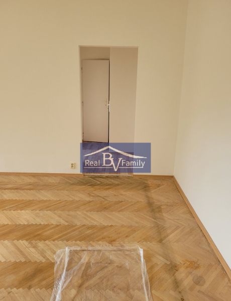 An empty room with wooden flooring in a 3-room apartment with open doors.