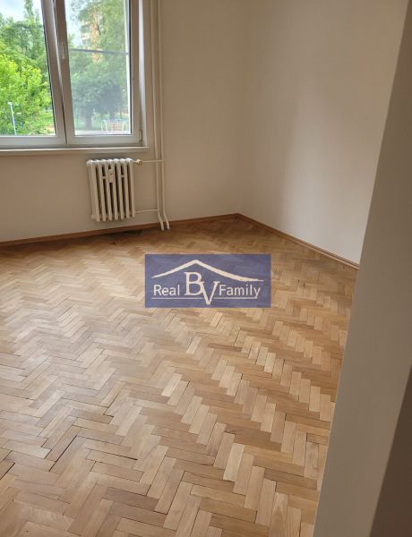 A room with wooden parquet and a radiator in a 3-room apartment with trees outside.