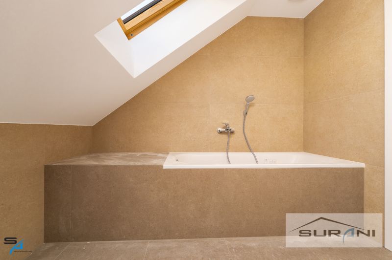 An attic bathroom with a bathtub and a skylight in a family house.