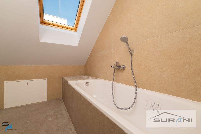 A bathroom in a family house with a bathtub under a skylight and beige tiles.