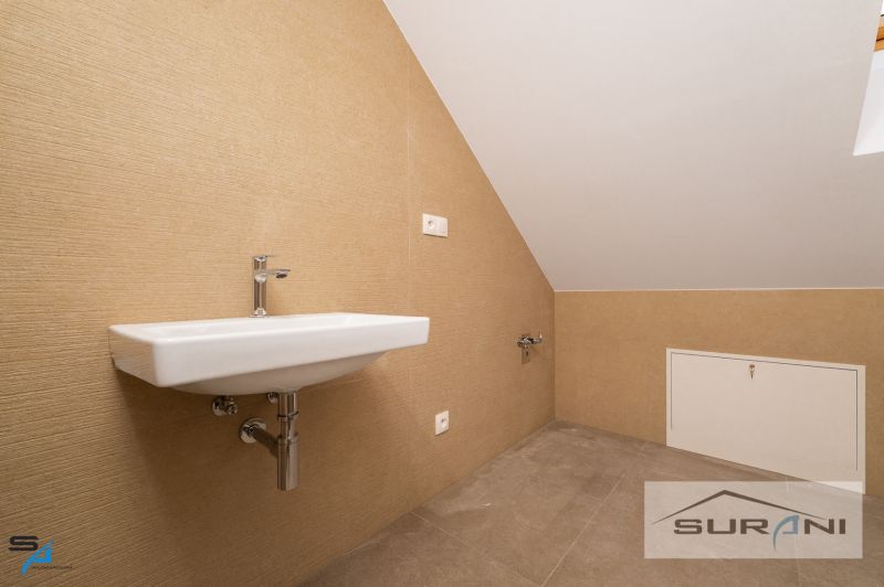 A sink in the attic bathroom of a family house with beige tiles and a sloped ceiling.