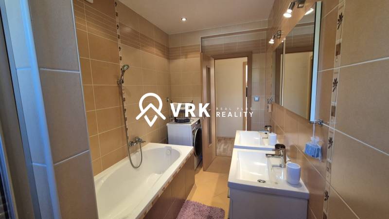 A bathroom in a family house with a bathtub, two sinks, and a washing machine, surrounded by brown tiles.