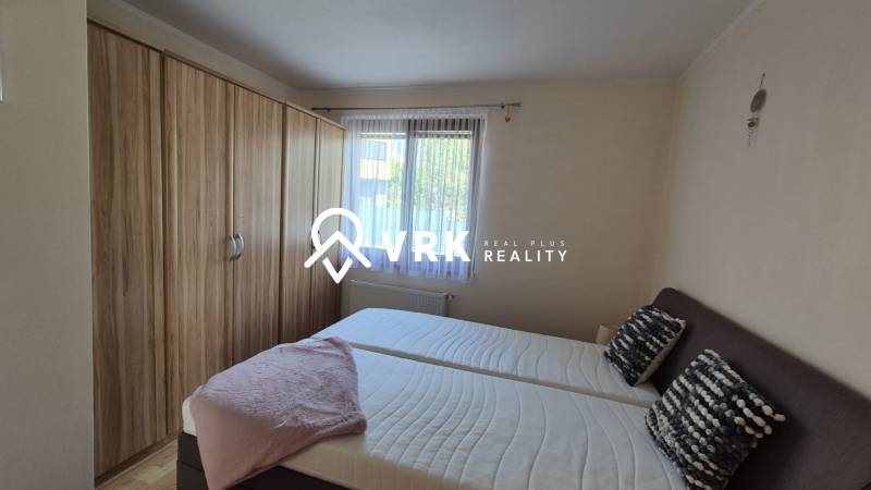 Bedroom in a family house with a bed, a large wardrobe, and a window with white curtains.