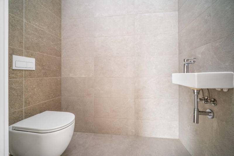 Toilet with a sink in a 4-room apartment, light tiles, minimalist design.