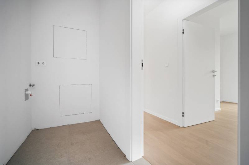 An empty room in a 4-room apartment with a wood-patterned floor and white walls.