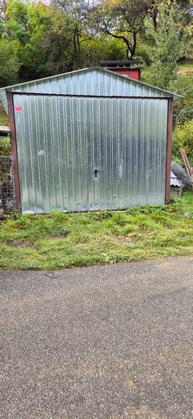 A metal garage by a family house on Škoruby Street in Kolárovce, surrounded by greenery.