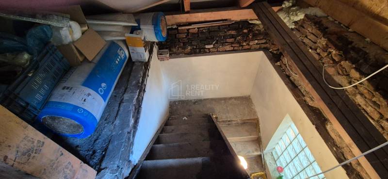 A basement in a family house with a staircase, a brick wall, and building materials.