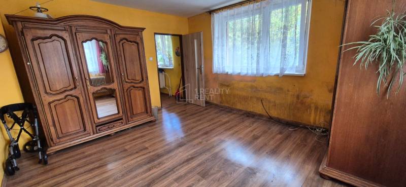 A room in a family house with a rustic wardrobe, a large window, and a floor with a wooden decor.
