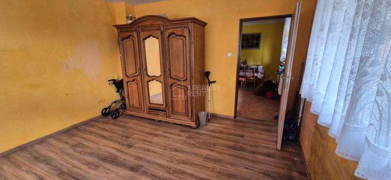 A room in a family house with a wooden wardrobe, a floor with a wooden decor, and light curtains.