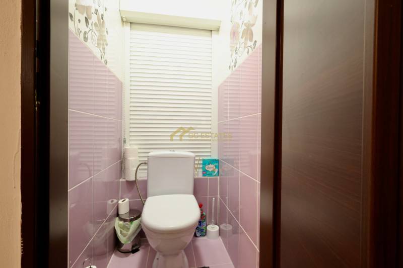 A bathroom in a one-room apartment with pink walls and blinds on the window.