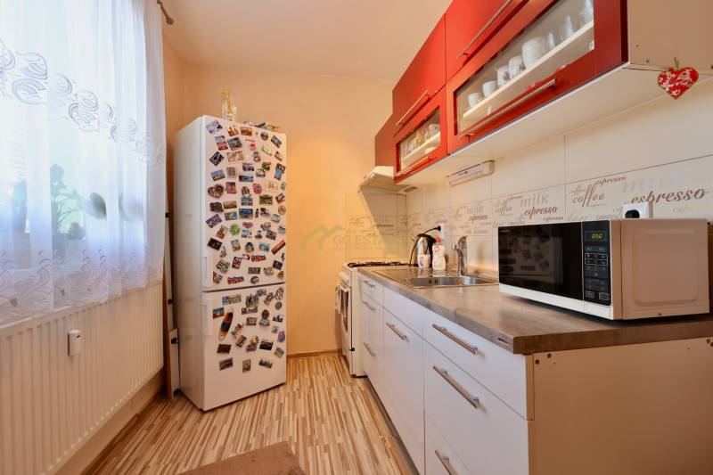 A kitchen in a studio apartment with red cabinets, a refrigerator, and a wooden decor floor.