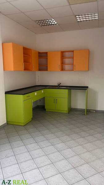 A kitchen unit with green and orange cabinets in an office on tiles.