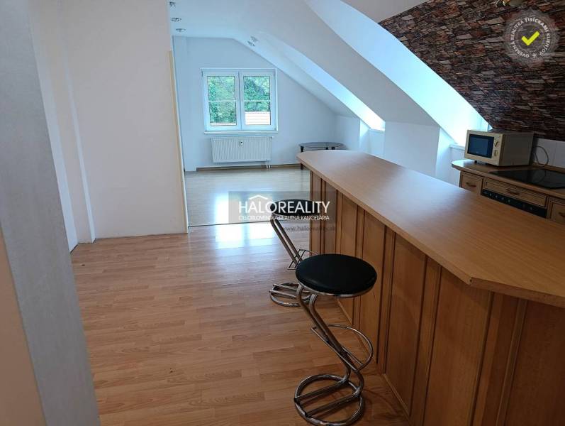 Two-room apartment with wood-patterned flooring, kitchen counter, and stools.