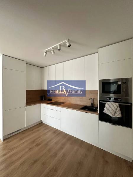 A kitchen in a 2-room apartment with a wooden decor floor, white cabinets, and built-in appliances.