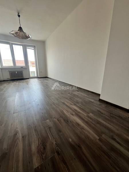 Living room in a three-room apartment with a wooden decor floor and a large window.