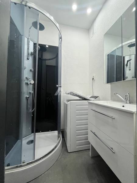 Bathroom in a 3-room apartment with a shower, washing machine, and sink with a mirror.