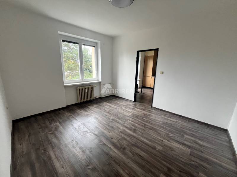 An empty room in a 3-room apartment with white walls and a floor with a wood decor.