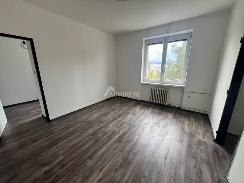 A room in a 3-room apartment with a wood-patterned floor and a large window.