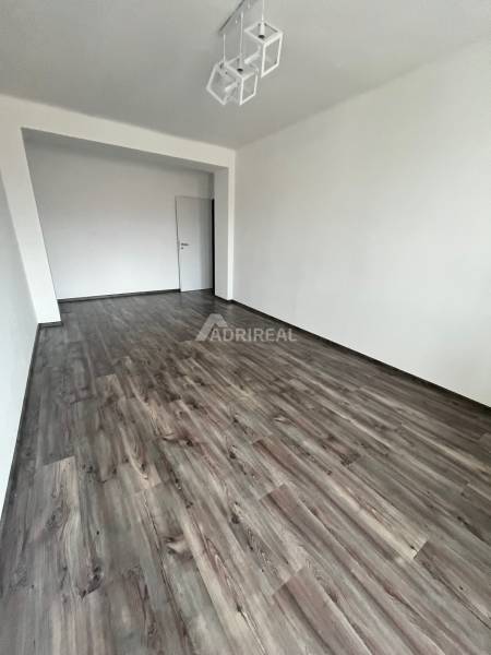 A spacious room with a wooden decor floor and white walls in a 3-room apartment.