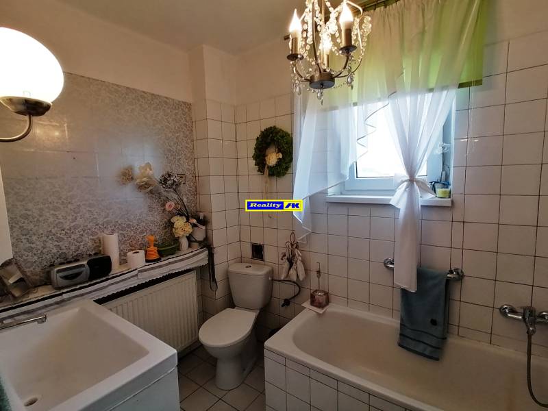 A bathroom in a 3-room apartment with a bathtub and a window, decorated with a curtain and flowers.