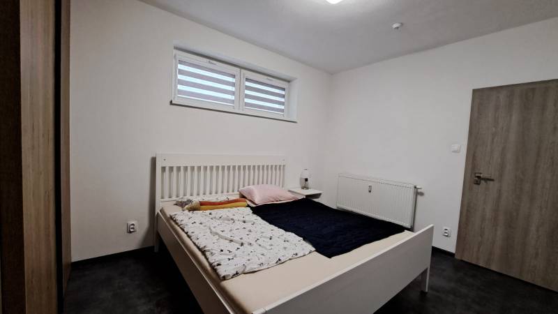 A bedroom with a gray floor in a 2-room apartment, a bed, and white walls.
