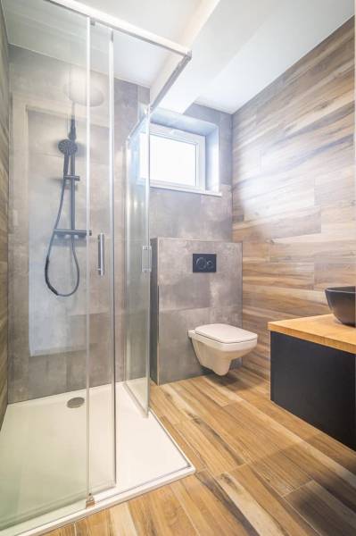 Bathroom in a 2-room apartment with a glass shower enclosure and a floor with a wooden decor.