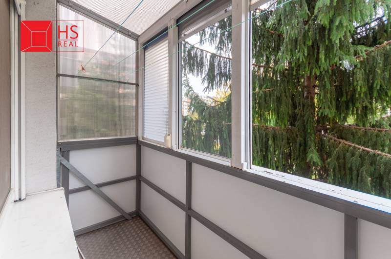 A glazed balcony of a 3-room apartment with a view of trees and clotheslines for drying laundry.