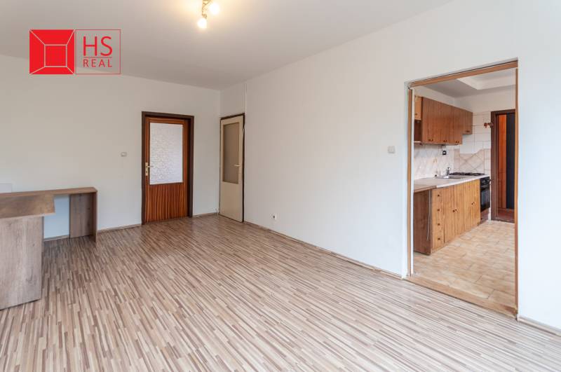 A room with a wooden decor floor and a kitchenette in a 3-room apartment.