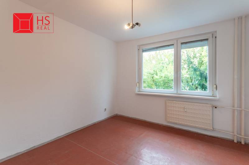 A room in a 3-room apartment with a window, white walls, and a floor with a wood decor.