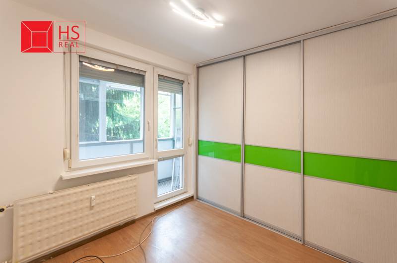 A room with a wooden decor floor, a built-in wardrobe, and balcony doors in a 3-room apartment.